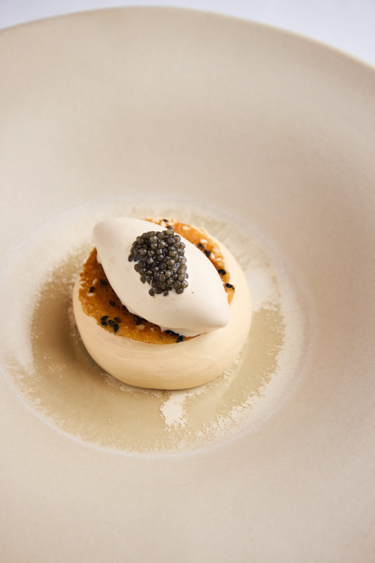 A gourmet dish featuring a round, creamy base topped with a dollop of white mousse and a small mound of black caviar, elegantly presented on a large white plate—perfect for those seeking exclusive dining offers.