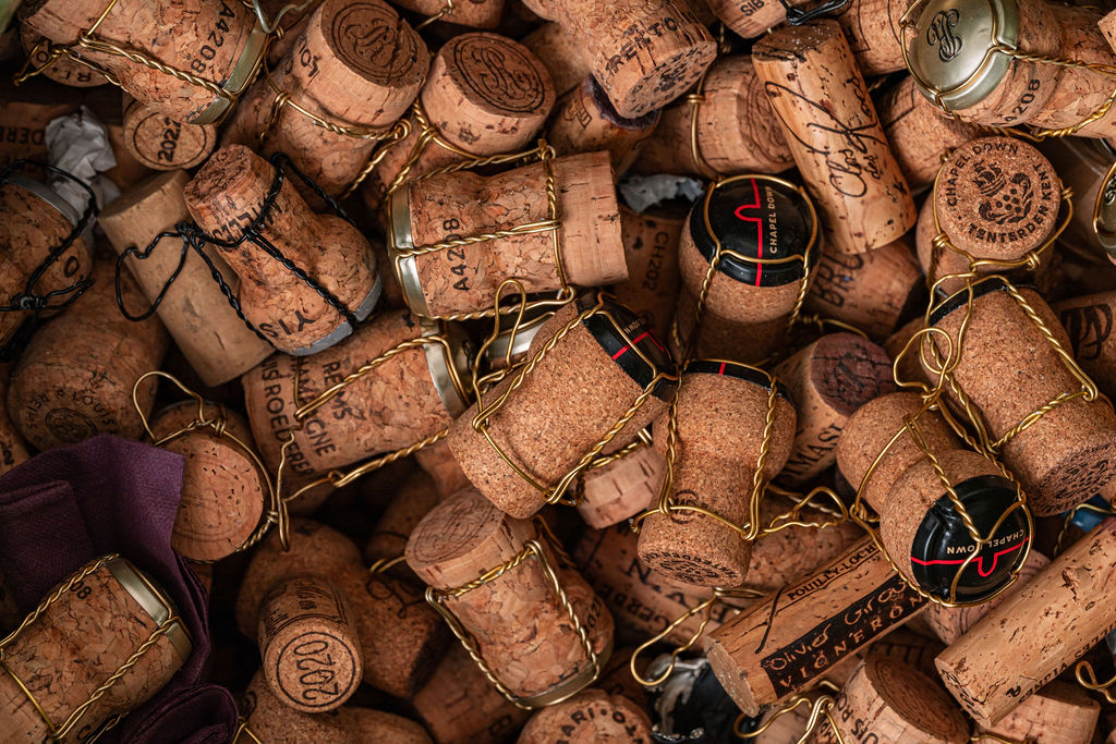A close-up of a pile of used champagne corks, some with metal wire cages still attached, scattered together—perfect remnants from a lively wine tasting. The corks display markings and logos from various brands.