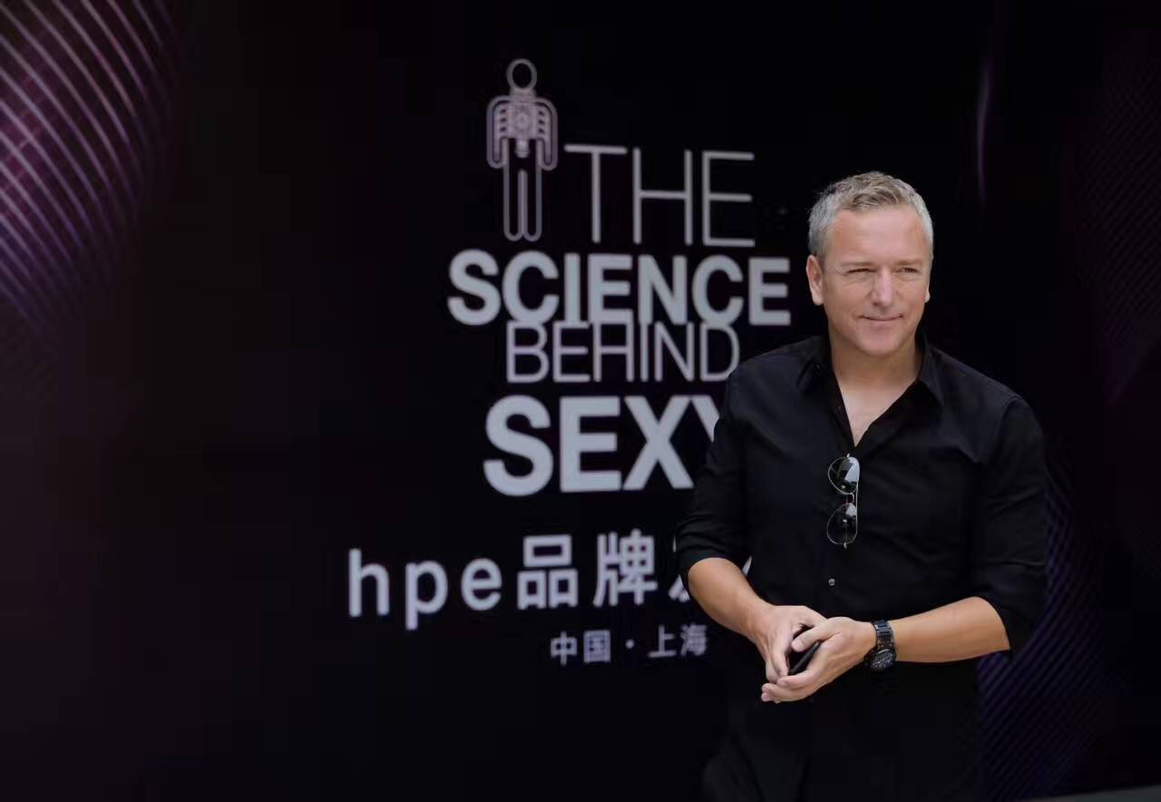 A man in a black shirt stands in front of a dark backdrop with the text THE SCIENCE BEHIND SEXY, hpe 品牌, and 中国·上海 written on it. The man is holding sunglasses and smiling slightly.