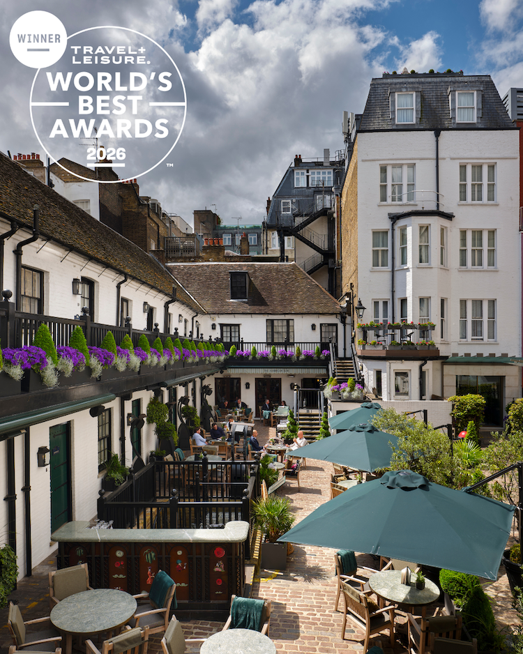 A charming courtyard with outdoor seating, green umbrellas, flower boxes, and historic white buildings. The Travel + Leisure Worlds Best Awards 2026 winner badge is displayed in the top left corner.