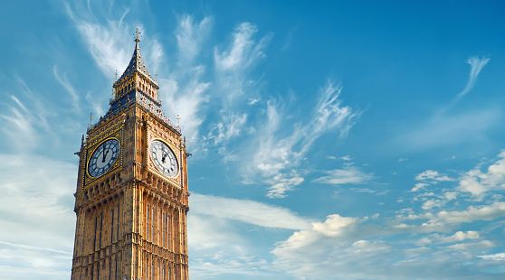 Big Ben clock tower in London against a bright blue sky with white clouds scattered in the background.