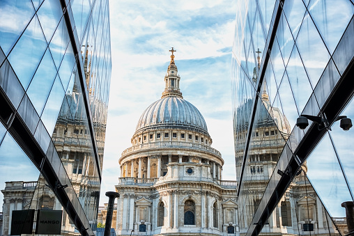 St. Paul’s Cathedral in London, centered between two modern glass buildings reflecting its dome on a bright, partly cloudy day.