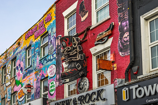 Colorful building facade with 3D shop signs, graffiti, and murals, including a large boot and musical elements, in Camden Market, London. Signs advertise coffee, gifts, and rock-themed shops.