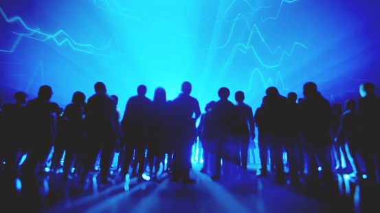 A group of people stand silhouetted against a bright blue background with abstract line graphs and light rays, creating a futuristic or tech-themed atmosphere.