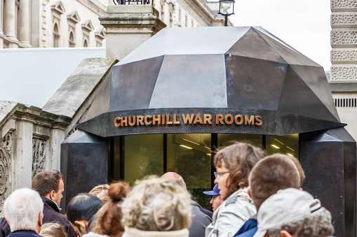A crowd gathers outside the entrance to the Churchill War Rooms, with the building’s modern, angular façade and sign visible.