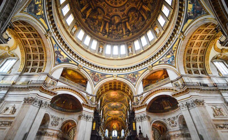 Interior view of a grand cathedral dome with ornate arches, columns, and detailed gold and fresco decorations, seen from below.