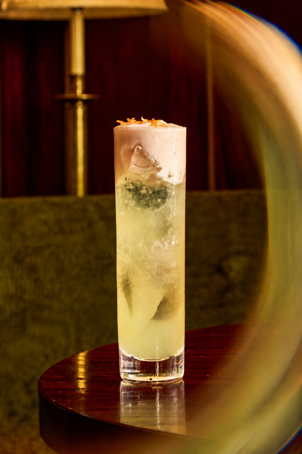 A tall Mother’s Day cocktail in a glass filled with ice, topped with a thick layer of froth and citrus zest.