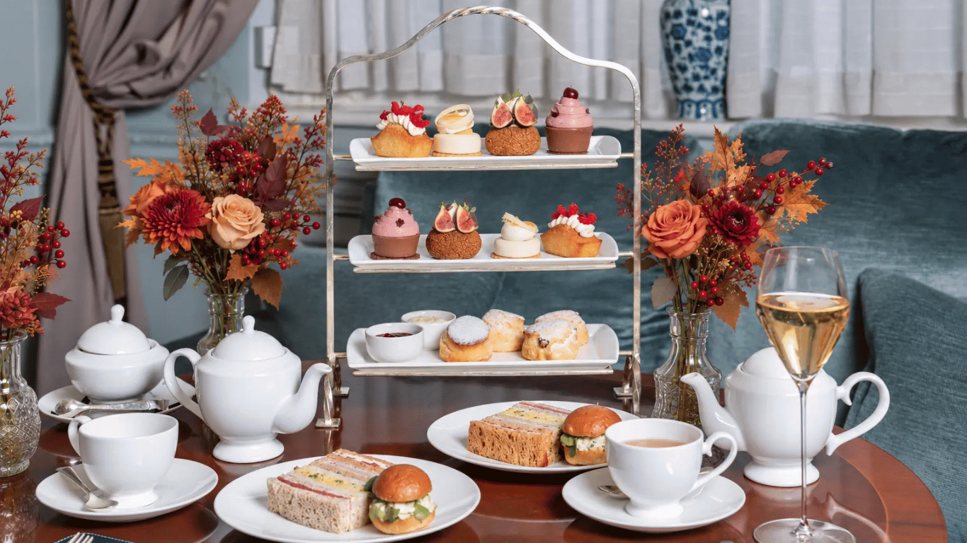 A three-tiered afternoon tea set featuring various pastries and scones, flanked by floral arrangements, teapots, cups, and plates of sandwiches on a table.